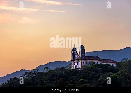 Alte und historische Kirche auf dem Hügel bei Sonnenuntergang in der Stadt Ouro Preto in Minas Gerais, Brasilien mit den Bergen hinter Ouro Preto Stockfoto