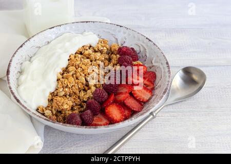 Hausgemachtes Müsli mit Erdbeerbrocken in einer hellen Platte und Joghurt in einem Glas. Auf einem hellen Hintergrund. Vegetarisches Gericht. Gesundes Frühstück. Speicherplatz kopieren. Stockfoto