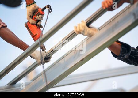 Ein Arbeiter verwendet eine Bohrmaschine, um eine Kappe Metalldach Job mit Schrauben zu befestigen. Stockfoto