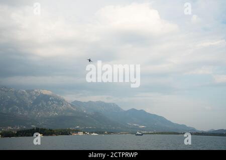 Blick auf die Berge und die Küstenstadt Montenegro an einem sommerlichen bewölkten Tag. Flugzeuge fliegen zwischen den Wolken, Yachten schwimmen auf dem Wasser. Da ist ein li Stockfoto
