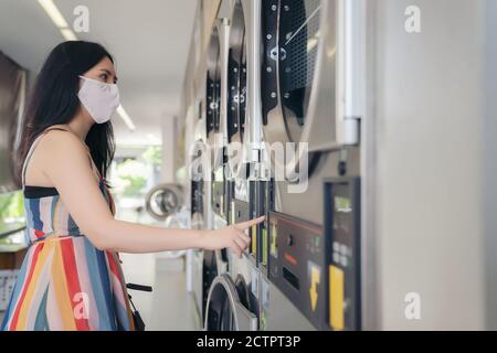 Schöne Frau mit Maske macht Wäsche im Waschsalon Shop. Stockfoto