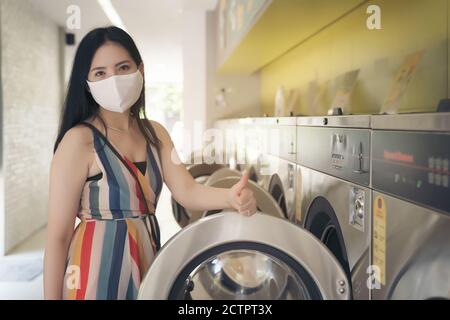 Schöne Frau mit Maske macht Wäsche im Waschsalon Shop. Stockfoto