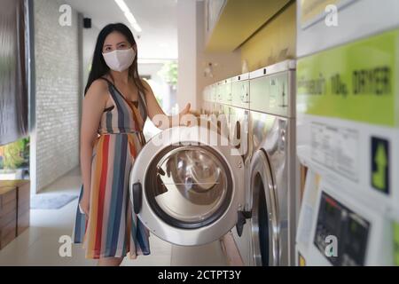 Schöne Frau mit Maske macht Wäsche im Waschsalon Shop. Stockfoto