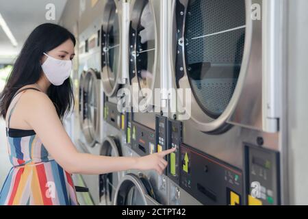 Schöne Frau mit Maske macht Wäsche im Waschsalon Shop. Stockfoto