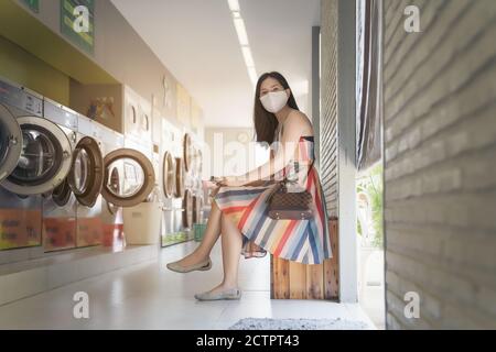 Schöne Frau mit Maske macht Wäsche im Waschsalon Shop. Stockfoto