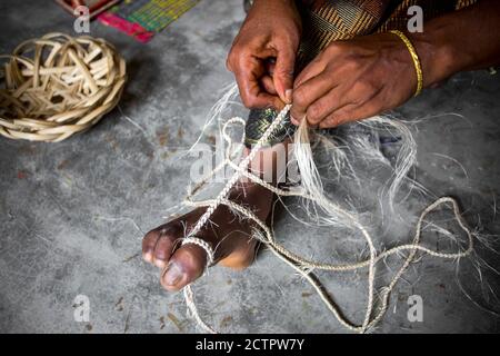 Eine Frau macht aus den Fasern einer Bananenstaude mit Hilfe ihrer Füße auf uralte Weise ein Seil in Madhupur, Tangail, Bangladesch. Stockfoto