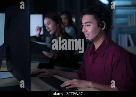Thailändischer asiatischer Mann Kundenbetreuungsunternehmen, die Nachtschicht im Callcenter für die Unterstützung des Kunden am Arbeitsplatz in der Nacht arbeiten, freundlich Stockfoto