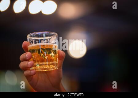 Nahaufnahme eines jungen Mannes, der ein Glas Wein an einer Theke im Pub hält. Das Licht leuchtet im Hintergrund, Weinprobe mit Kopierraum. Stockfoto