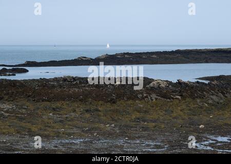 Blick auf ein Segelboot am Horizont und Meer am 15. September 2020 in Cemlyn, Anglesey, Wales, Vereinigtes Königreich. Cemlyn ist eine Bucht an der Nordwestküste von Anglesey, Nordwales, innerhalb der Gemeinschaft von Cylch-y-Garn. Von der Bucht durch einen Kiesstrand getrennt ist eine Bracklagune, die von einer Reihe kleiner Bäche gespeist wird. Stockfoto