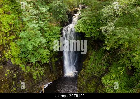 Luftdrohne Ansicht eines hohen Wasserfalls in einem engen Canyon umgeben von Bäumen (Sgwd Dinion Gam, Wales, UK) Stockfoto