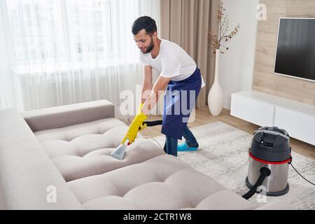 Nahaufnahme der Haushälterin hält modernen Waschsauger und Reinigung schmutzige Sofa mit professionell Reinigungsmittel. Professioneller Springclean zu Hause Stockfoto