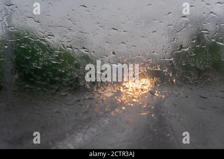 Tropfen aus dem Regen auf die Windschutzscheibe am Abend, in die Hintergrundbeleuchtung des entgegenkommenden Autos Stockfoto