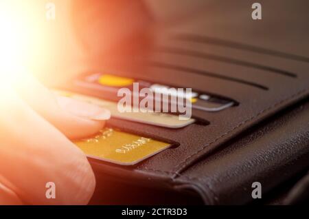 Die Hand der Frauen zieht eine Kreditkarte aus einer schwarzen Handtasche. Foto mit Lichtreflexionen Stockfoto