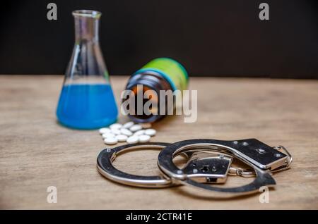 Handschellen, Kolben und Pillen auf schwarzem Hintergrund. Das Konzept der Medizin und Expertise Stockfoto