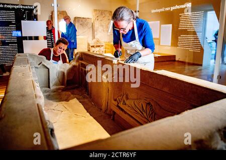 Mitarbeiter, die während der Restaurierung am Sarkophag arbeiten.EIN zerbrochener römischer Sarkophag im Nationalmuseum der Altertümer in Leiden wird restauriert. Die 2.5 Meter lange Sandsteinkiste wurde 1930 bei Simpelveld in Limburg gefunden. Frühere Forschungen über das Knochenmaterial haben festgestellt, dass die eingeäscherte Frau zwischen 35 und 50 Jahre alt war, als sie starb und ein gutes Leben ohne harte Arbeit geführt hatte. Stockfoto