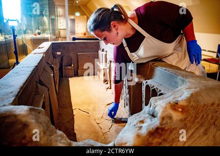 Ein Mitarbeiter, der während der Restaurierung am Sarkophag arbeitet.EIN zerbrochener römischer Sarkophag im Nationalmuseum der Altertümer in Leiden wird restauriert. Die 2.5 Meter lange Sandsteinkiste wurde 1930 bei Simpelveld in Limburg gefunden. Frühere Forschungen über das Knochenmaterial haben festgestellt, dass die eingeäscherte Frau zwischen 35 und 50 Jahre alt war, als sie starb und ein gutes Leben ohne harte Arbeit geführt hatte. Stockfoto