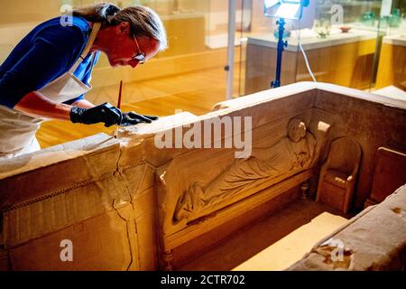 Ein Mitarbeiter, der während der Restaurierung am Sarkophag arbeitet.EIN zerbrochener römischer Sarkophag im Nationalmuseum der Altertümer in Leiden wird restauriert. Die 2.5 Meter lange Sandsteinkiste wurde 1930 bei Simpelveld in Limburg gefunden. Frühere Forschungen über das Knochenmaterial haben festgestellt, dass die eingeäscherte Frau zwischen 35 und 50 Jahre alt war, als sie starb und ein gutes Leben ohne harte Arbeit geführt hatte. Stockfoto