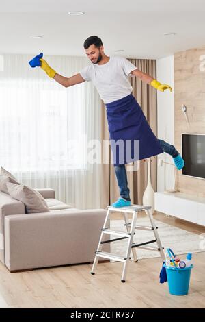Mann hat Spaß beim Klettern Leiter zu reinigen Decke. Reinigungsdienstkonzept Stockfoto