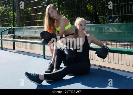 Sportliche Frauen und Mädchen Modelle sitzen und posieren im Boxen Handschuhe auf Sportplatz an sonnigen Tag Stockfoto