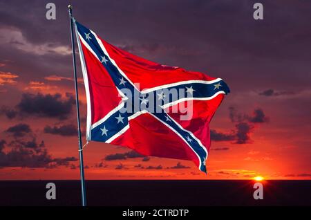 Spektakulärer Sonnenaufgang hinter einer konföderierten Flagge, die im Wind weht Gegen einen Sonnenhimmel Stockfoto