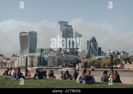 London, Großbritannien - 25. August 2020: Menschen, die am Südufer der Themse gesellschaftlich distanziert sitzen, City of London, einem historischen Finanzviertel, Stockfoto