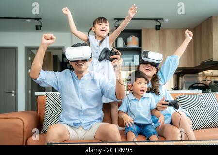 Glückliche asiatische Familie zu Hause auf Wohnzimmer Sofa mit Spaß, während sie aussehen Mutter und Vater spielen Mit Virtual Reality Headset VR in l Stockfoto