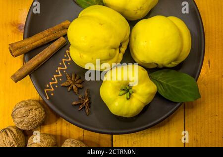 Große gelbe Quinzfrüchte auf einer Keramikplatte mit Anis, Zimt und Walnüssen Stockfoto