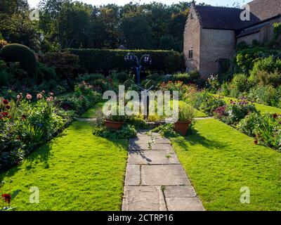 Chenies Manor House versunkener Garten an einem sonnigen Septembernachmittag. Bunte Dahlien in krautigen Pflanzengrenzen, Skulpturen und Zierteich. Stockfoto