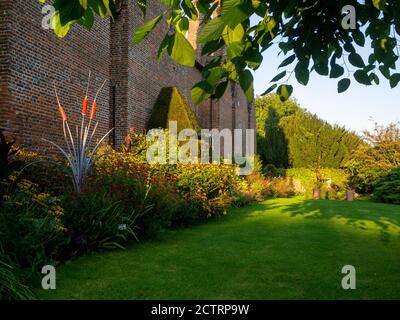 Chenies Manor House SW Wall an einem sonnigen Septembernachmittag, 2020. Krautige Pflanzengrenzen, Rasen, eingerahmt von Maulbeerbaum. Jenny Pickfords Skulptur. Stockfoto