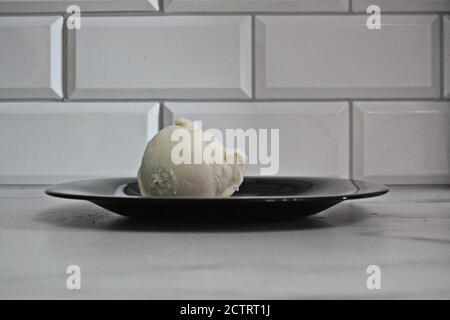 Eine Kugel Vanilleeis auf einem schwarzen Teller Stockfoto