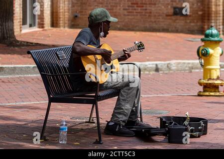 Annapolis, MD 08/21/2020: Ein älterer afroamerikanischer Mann, der Baseballhut und eine Gesichtsmaske trägt, spielt klassische Gitarre und singt, während er o sitzt Stockfoto