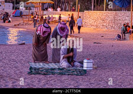 Aqaba, Jordanien 03/31/2010: Drei arabische Männer in ethnischer Kleidung führen das Abendgebet auf traditionellen Teppichen am Strand am Golf von Stockfoto