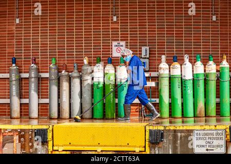 Bethesda, MD, USA 09/15/2020: Ein Hausmeister mit Haarmütze, blauen Peelings, Plastikstiefeln, Gesichtsmaske und Handschuhen putzt eine Laderampe einer Arbeitsstelle Stockfoto