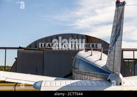 Indian Head, MD, USA 09/19/2020: 'Learn to Fly Here' auf einem verrosteten Flughafenhangar im lokalen Flughafen Maryland (2w5). Ein Piper PA-28 Cherokee Sing Stockfoto