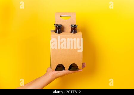 Hand hält eine vierpackige Bierpräsentation mit gelbem Hintergrund Stockfoto