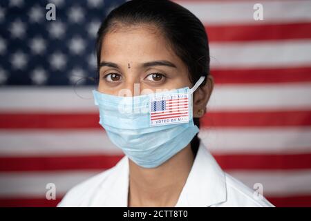 Close up Face of Girl with Ich habe mit dem Hauptaufkleber auf ihrer medizinischen Maske mit US-Flagge als Hintergrund gestimmt - Konzept der Post bei der Wahl in den USA. Stockfoto