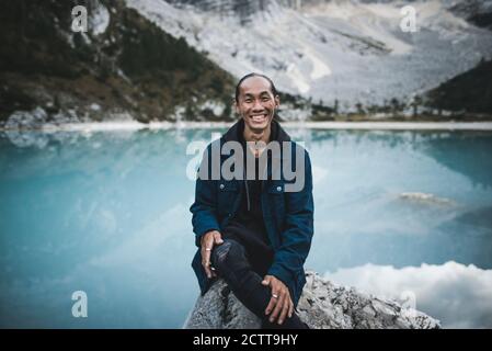 Italien, Südtirol, Cortina d Ampezzo, Sorapis-See, Portrait des jungen Mannes, der auf Felsen am Bergsee sitzt Stockfoto