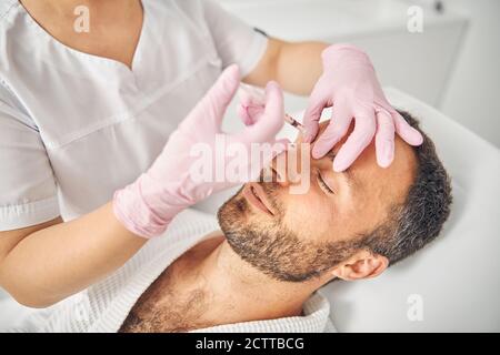 Lächelnder junger Mann, der kosmetische Injektionen im Wellnesscenter erhält Stockfoto