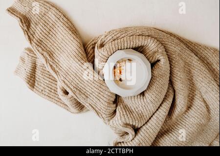 Kerze mit getrockneten Blumen in Beton Vase in gemütlichen beige gestrickten Pullover auf weißem Hintergrund eingewickelt, selektive Fokus Stockfoto