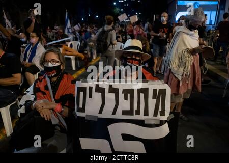 JERUSALEM, ISRAEL – 24. SEPTEMBER 2020: Ein Protestler hält ein Plakat mit der Aufschrift "Wir beten, geh weg", während Demonstranten auf Stühlen sitzen, die den sozialen Distanzierungsregeln folgen, während einer Demonstration vor Benjamin Netanjahus offiziellem Wohnsitz inmitten einer landesweiten Sperre, die darauf abzielt, die Coronavirus-Pandemie am 24. September 2020 in Jerusalem, Israel, einzudämmen. Eine Welle von Protesten hat Israel in den letzten Monaten überschwemmt, um Netanjahus Rücktritt wegen seiner Anklage wegen Korruptionsvorwürfen und des Umgangs mit der Coronavirus-Pandemie zu fordern. Stockfoto