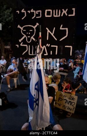 JERUSALEM, ISRAEL – 24. SEPTEMBER 2020: Ein Protestler hält ein Plakat mit der Aufschrift "der kriminelle Angeklagte ist nicht mein Premierminister", während Demonstranten auf Stühlen sitzen, die den sozialen Distanzierungsregeln folgen, während einer Demonstration vor Benjamin Netanjahus offiziellem Wohnsitz inmitten einer landesweiten Sperre, die darauf abzielt, die Coronavirus-Pandemie am 24. September 2020 in Jerusalem, Israel, einzudämmen. Eine Welle von Protesten hat Israel in den letzten Monaten überschwemmt, um Netanjahus Rücktritt wegen seiner Anklage wegen Korruptionsvorwürfen und des Umgangs mit der Coronavirus-Pandemie zu fordern. Stockfoto