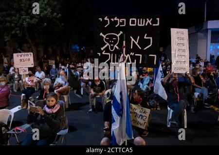 JERUSALEM, ISRAEL – 24. SEPTEMBER 2020: Ein Protestler hält ein Plakat mit der Aufschrift "der kriminelle Angeklagte ist nicht mein Premierminister", während Demonstranten auf Stühlen sitzen, die den sozialen Distanzierungsregeln folgen, während einer Demonstration vor Benjamin Netanjahus offiziellem Wohnsitz inmitten einer landesweiten Sperre, die darauf abzielt, die Coronavirus-Pandemie am 24. September 2020 in Jerusalem, Israel, einzudämmen. Eine Welle von Protesten hat Israel in den letzten Monaten überschwemmt, um Netanjahus Rücktritt wegen seiner Anklage wegen Korruptionsvorwürfen und des Umgangs mit der Coronavirus-Pandemie zu fordern. Stockfoto