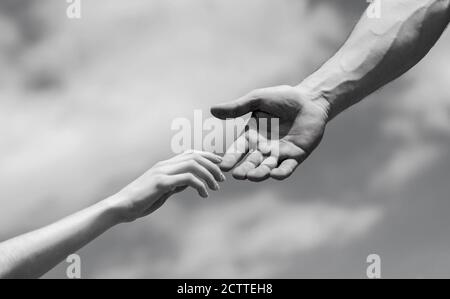 Eine helfende Hand geben. Hände von Mann und Frau auf blauem Himmel Hintergrund. Eine helfende Hand geben. Solidarität, Mitgefühl und Nächstenliebe, Rettung. Schwarz und Stockfoto