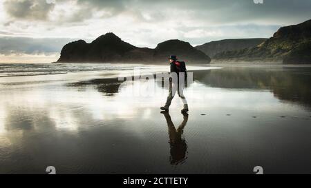 Wandern am Strand von Bethells mit Spiegelung auf dem nassen schwarzen Sand, Waitakere, Auckland Stockfoto