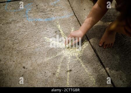 Geringe Schärfentiefe (selektiver Fokus) Bild mit einem Mädchen, das auf Betonavement mit farbiger Kreide zeichnet. Stockfoto