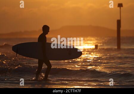 Ein Surfer geht ins Meer, während die Sonne über Boscombe Beach in Dorset aufgeht. Stockfoto