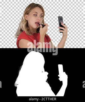 Blonde Frau Anwendung Lippenstift suchen im Telefon, Alpha Chann Stockfoto