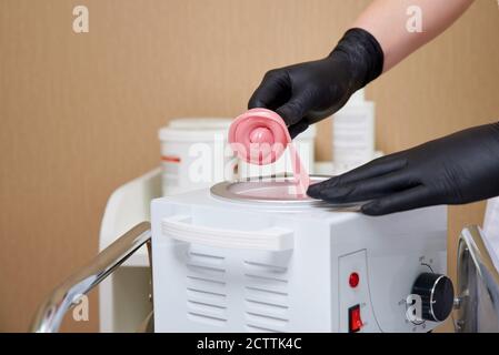 Wachserhitzer mit heißem gelbem Wachs auf Holzspatel in menschlicher Hand. Heißes Wachs für Enthaarung. Salonausstattung Stockfoto