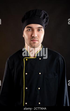 Porträt von jungen in einem schwarzen Koch Anzug posiert gekleidet Auf braunem Hintergrund mit Werbungsfläche Stockfoto