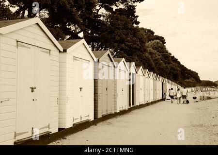 MUDEFORD, ENGLAND, UK - 26. AUGUST 2017: Menschen mit Hund wandern am Avon Beach mit seinen malerischen Holzhütten am Abend entlang. Stockfoto